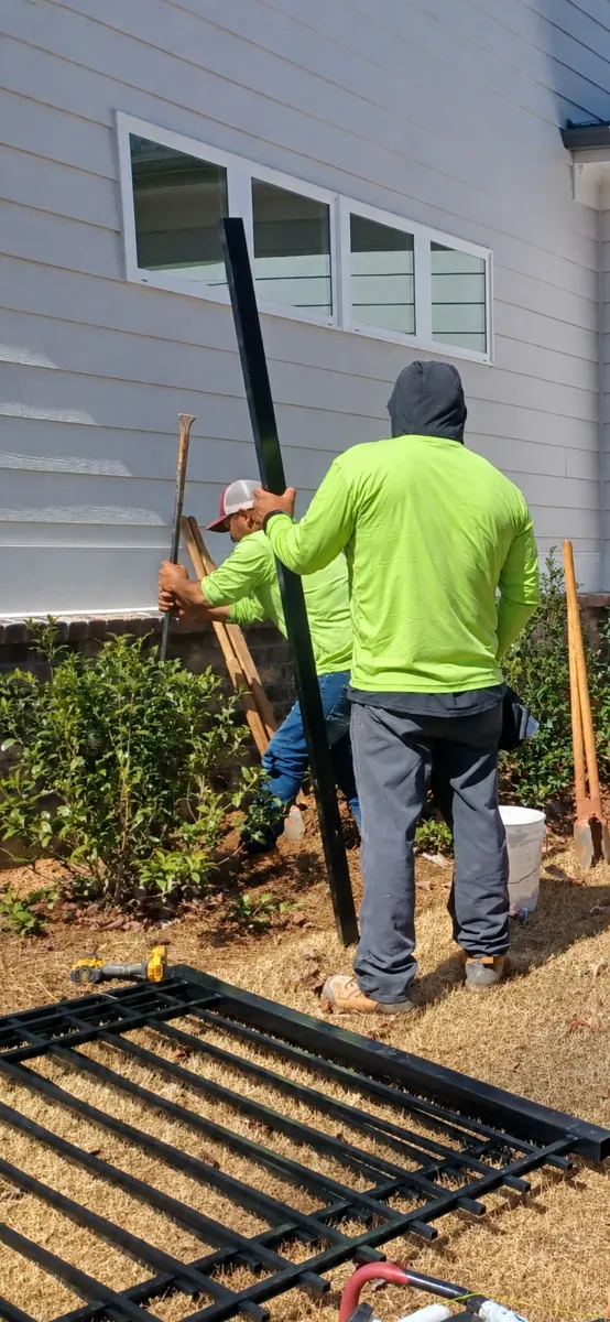 Fence crew setting an aluminum gate post beside a home