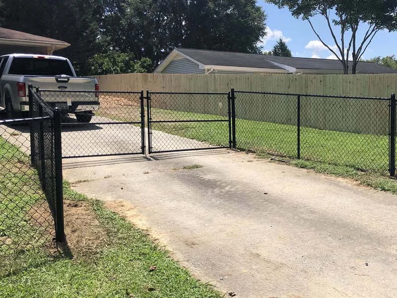 Chain-link vehicle opening beside a driveway